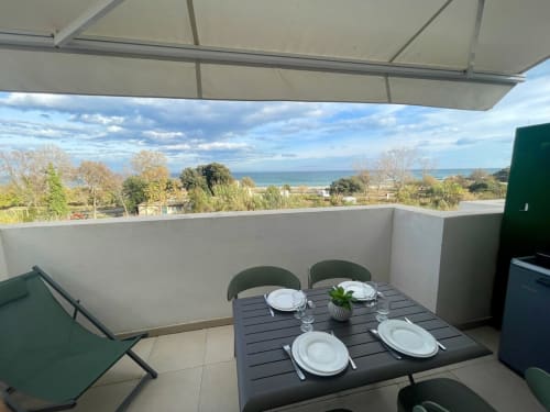 Terrasse en bord de mer à la Résidence Marina di Bravone avec vue sur la mer, table à manger dressée pour les clients, store rétractable et