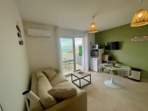 Appartement lumineux à la Résidence Marina di Bravone avec balcon vue mer, canapé beige, kitchenette, mur d'accent vert et design moderne