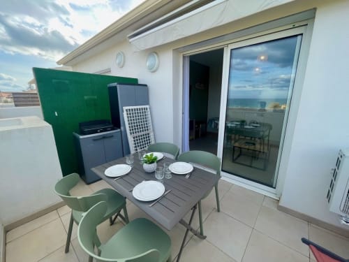 Terrasse d'appartement côtier à la Résidence Marina di Bravone avec vue mer, table à manger, chaises vertes, kitchenette