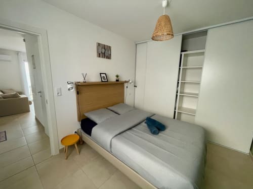 Chambre lumineuse à la Résidence Marina di Bravone avec lit queen-size, tête de lit en bois, luminaire suspendu tressé et rangements intégrés