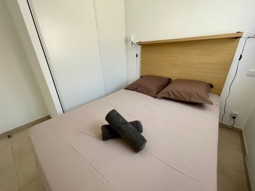 Camera moderna con testata in legno, biancheria rosa, cuscini marrone e asciugamani arrotolati a Résidence Marina di Bravone