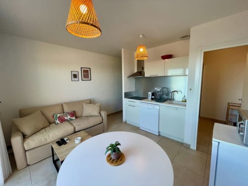 Moderno appartamento a Résidence Marina di Bravone con divano beige, cucina bianca, tavolo rotondo e lampade a sospensione intrecciate