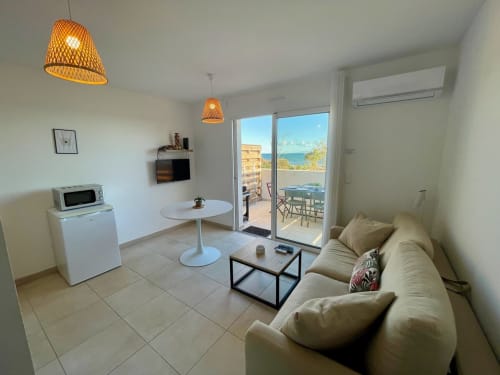 Moderno soggiorno con vista mare, terrazza, divano beige e lampade in vimini a Résidence Marina di Bravone