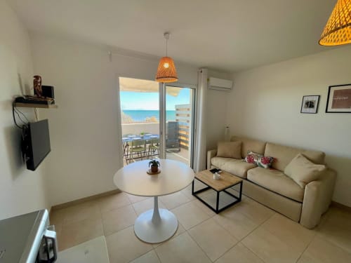 Appartamento fronte spiaggia Marina di Bravone con balcone vista mare, soggiorno con divano, tavolo rotondo e illuminazione al tramonto costiero
