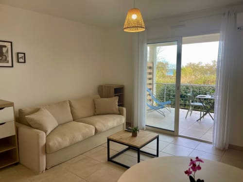 Moderno monolocale a Résidence Marina di Bravone con divano beige, tavolo in legno e terrazza con vista mare a Linguizzetta
