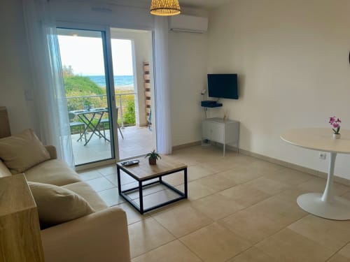 Elegante monolocale con vista mare alla Résidence Marina di Bravone, con divano beige, TV e balcone fronte oceano