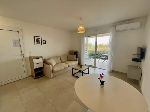 Moderno monolocale a Résidence Marina di Bravone con divano beige, tavolo rotondo e balcone con vista sul mare