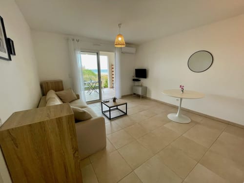 Luminoso monolocale a Marina di Bravone con vista mare, divano beige, specchio rotondo e balcone affacciato sull'acqua