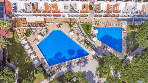 Vista aérea del resort HomyMarbella en Elvira con dos piscinas azules, playa arenosa, palmeras y frente de playa