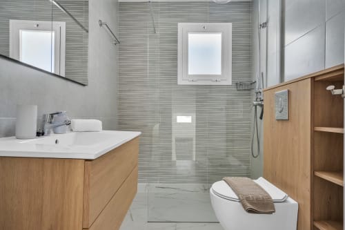 Baño moderno de la casita HomyMarbella en Marbella con tocador de madera, ducha de cristal, inodoro y pisos de azulejos blancos