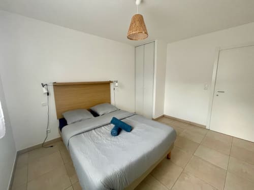 Chambre moderne à la Résidence Marina di Bravone avec lit en bois, luminaire suspendu tressé et carrelage