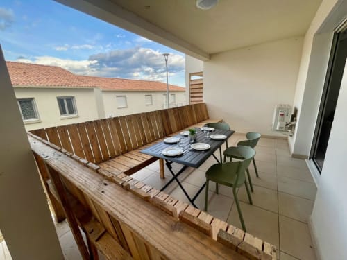 Balcon d'appartement face à la mer à la Résidence Marina di Bravone avec table à manger, chaises vertes, garde-corps en bois et vue côtière