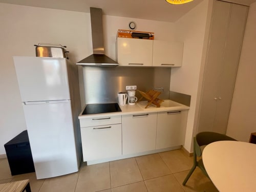 Petite kitchenette avec armoires blanches, hotte aspirante en acier inoxydable et réfrigérateur blanc à la Résidence Marina di Bravone,