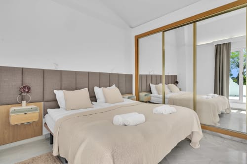 Dormitorio moderno en la casita HomyMarbella de Elviria con armario espejado, cabecero tapizado gris y acceso a balcón