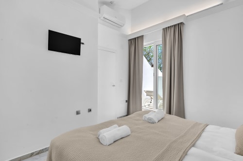 Dormitorio moderno en la casa rural HomyMarbella Marbella con TV montada en pared, ropa de cama beige y puertas de patio