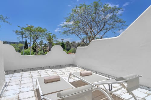 Soleada terraza en la azotea de la casita HomyMarbella en Elvira con tumbonas, muros blancos y hermosas vistas de los jardines circundantes
