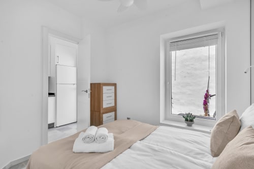 Dormitorio luminoso en cottage HomyMarbella con cama, armario de madera, amplio ventanal con vistas a Elviria y toallas enrolladas