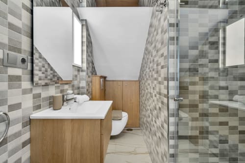 Baño moderno en cottage de Marbella con paredes de azulejos grises, tocador de madera, inodoro y ducha abierta en resort HomyMarbella.