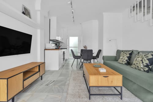 Luminosa sala de estar de planta abierta en la cabaña HomyMarbella de Elvíria con sofá color salvia, muebles de madera, cocina y comedor