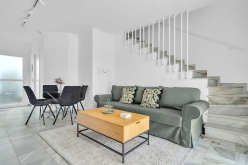 Salón moderno en la casa HomyMarbella de Marbella con sofá gris, mesa de madera, sillas negras y escalera