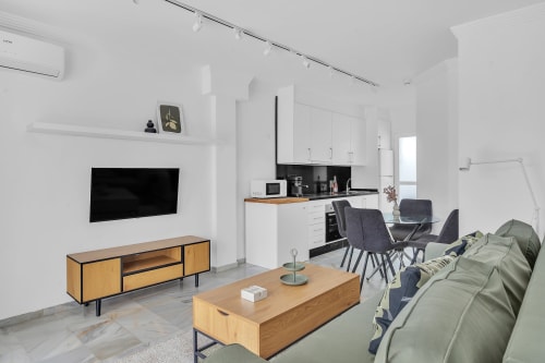 Salón comedor de planta abierta en casa de Marbella con TV, zona de comedor y sofá verde salvia.