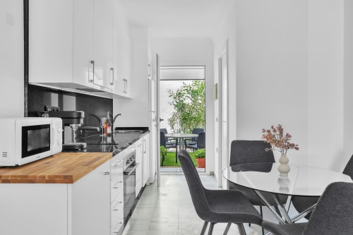 Moderna cocina blanca con encimera de madera, electrodomésticos negros, zona de comedor y vista al jardín en la casita HomyMarbella