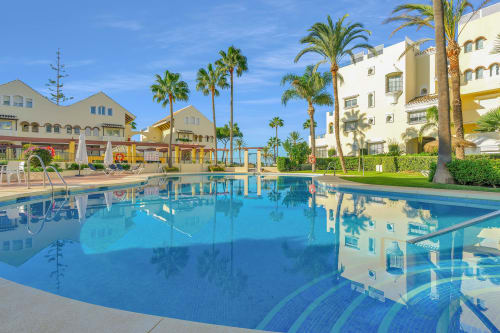 Sparkling pool at HomyMarbella Elviria with palm trees, white Mediterranean buildings, and garden views