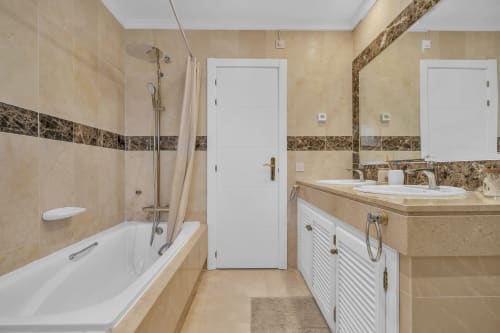 Modern bathroom at Casa Perla Marbella with beige tiles, white vanity, bathtub, shower, and decorative border trim