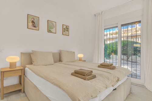Bright bedroom at HomyMarbella in Elviria with beige bedding, wooden nightstand, and garden view doors