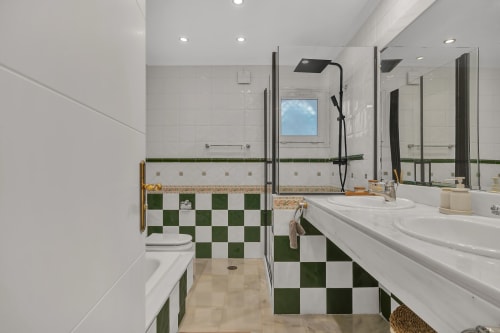 Modern bathroom at Casa Perla Marbella with green and white checkered tiles, dual sinks, walk-in shower, and skylight window.