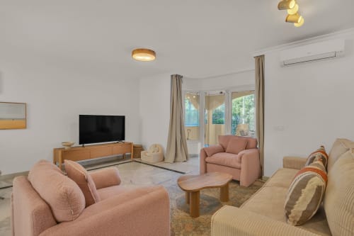 Spacious living room at Casa Perla Marbella with pink sofas, wooden TV stand, and garden view doors in Elviria