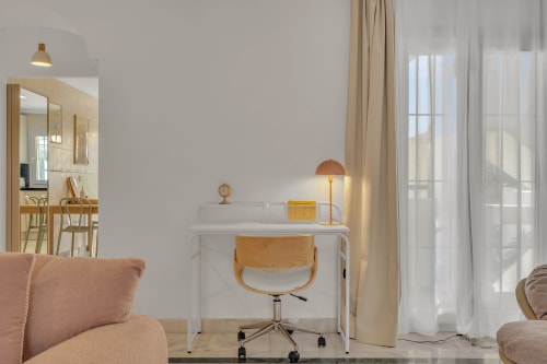 Modern apartment workspace at HomyMarbella Elviria with white desk, wooden chair, and garden view through sheer curtains