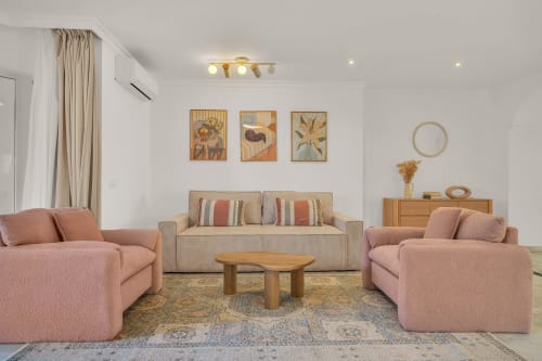 Bright living room at Casa Perla Marbella with pink armchairs, beige sofa, wooden table, and botanical artwork