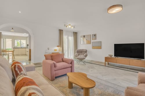 Modern apartment living room at Casa Perla Marbella with pink armchair, wooden coffee table, and flat-screen TV in Elviria,
