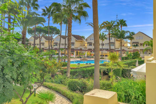 Garden view of HomyMarbella apartment in Elviria with palm trees, pool, and yellow Mediterranean buildings