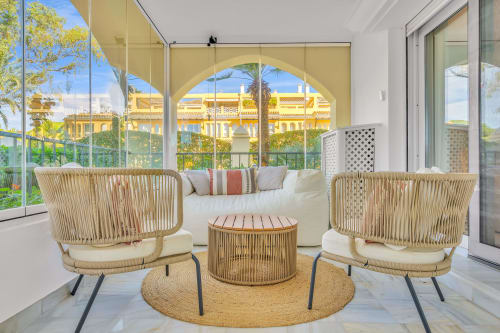 Luxury apartment terrace at HomyMarbella Elviria with woven chairs, garden views, and Mediterranean architecture overlooking