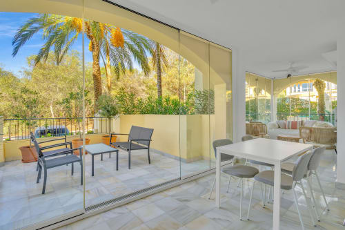Modern apartment balcony with seating at HomyMarbella in Elviria, Spain, overlooking palm trees and garden views