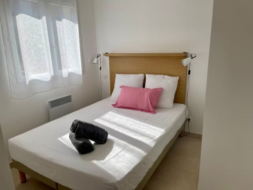 Bright bedroom at Résidence Marina di Bravone with wooden headboard, white bedding, pink pillow, and beach view through