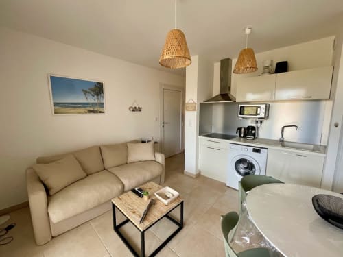 Cosy T2 apartment at Marina di Bravone with beige sofa, kitchenette, dining area, and beach view artwork