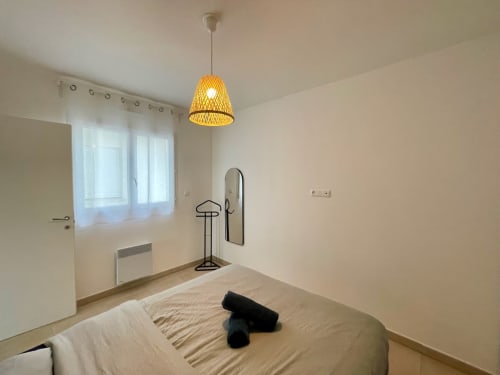 Bright bedroom at Résidence Marina di Bravone with woven pendant lamp, mirror, heater, and window view in Linguizzetta