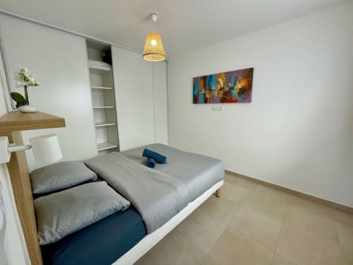 Camera moderna presso Résidence Marina di Bravone con letto gemellare, arredamenti in legno, lampada a sospensione intrecciata e arte murale colorata.