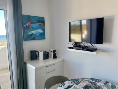 Camera d'albergo con vista mare, TV a parete, angolo cottura con bollitore e quadri di barche colorate a Marina di Bravone, Corsica