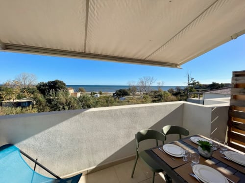 Terrazza della Résidence Marina di Bravone con vista mare, tavolo da pranzo, sedie, tenda da sole e piscina a Linguizzetta