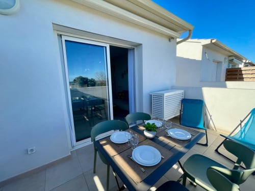 Terrazza soleggiata con tavolo apparecchiato, vista sul mare e elegante edificio bianco presso la Résidence Marina di Bravone a Linguizzetta