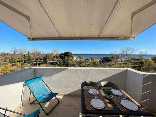 Terrazza della Résidence Marina di Bravone con tavolo da pranzo, poltrona blu e vista sul mare della Corsica