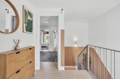 Nowoczesny hol w townhouse HomyMarbella z drewnianą komodą, okrągłym lustrem, obrazem z rośliną i schodami z metalową balustradą