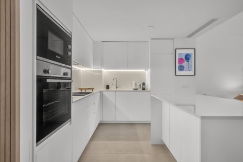 Nowoczesna biała kuchnia w townhouse HomyMarbella z wbudowanymi urządzeniami, wyspą kuchenną i minimalistycznym designem