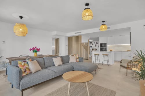 Nowoczesny salon open-plan z szarą sofą, drewnianym stołem jadalnym i wiszącymi lampami z plecionką w pensjonacie HomyMarbella w Elvirii