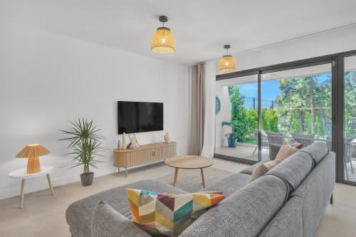 Nowoczesny salon domu w Marbelli z szarą sofą, drewnianym stojakiem na TV, lampami wiszącymi i widokiem na ogród przez drzwi przesuwne
