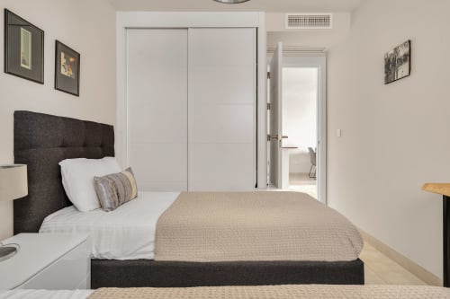 Nowoczesna sypialnia w apartamencie HomyMarbella w Elvirii z ciemnym zagłówkiem, białą pościelą i dostępem do łazienki